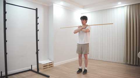 Video of a young man in a white T-shirt and beige shorts practicing the violin in a minimalist, brightly lit room with light wooden floors and white walls.