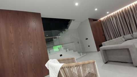 Video of a modern living room with a light gray sofa, wooden wall panels, and a minimalist design. A white chair and a white paper towel are in the foreground.