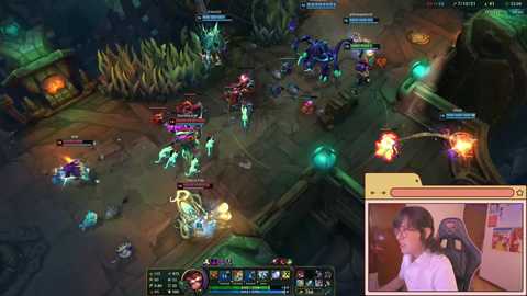 A screenshot from a video game, \"League of Legends,\" shows a vibrant, multi-colored arena with glowing, animated characters. A live stream in the bottom right features a young woman with glasses and a white shirt.