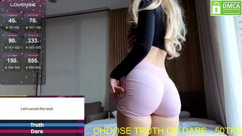 Video of a blonde woman in tight pink shorts and a black crop top, standing indoors with a dimly lit background, overlaid with a \"Truth or Dare\" game screen.