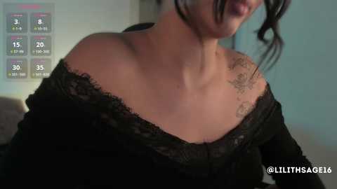 A close-up video of a woman with fair skin and dark hair, wearing an off-shoulder black lace top, revealing a floral tattoo on her shoulder. Background shows a digital health monitoring screen with vital signs.