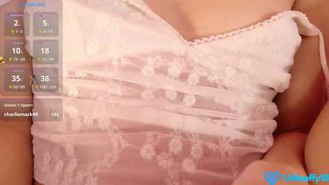 Video of a woman in a sheer, white lace dress with floral patterns, showing cleavage. A digital overlay displays menstrual cycle information, including dates and phases.