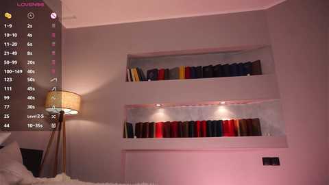 Video of a modern, minimalist bedroom with a beige bed and a white wall featuring two built-in shelves holding books and a lamp on the left.