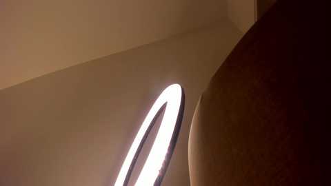 A video of a modern, minimalist interior space featuring a bright, circular LED light fixture hanging from the ceiling, casting a soft glow on a smooth, beige wall.