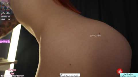 Video of a nude woman with fair skin, large buttocks, and a mole on her left cheek, taken indoors with dim lighting, displaying her profile.