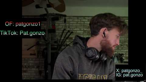 A video of a bearded man with short brown hair, wearing a hoodie and large headphones, sitting in a dimly lit room with a brick wall and a fan. Text overlay includes usernames and TikTok mentions.