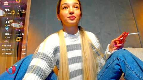 Video of a young woman with long blonde hair, wearing a striped sweater and blue jeans, sitting on a couch, holding a cigarette, with a virtual reality app interface in the background.