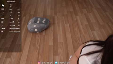 Video of a person with dark hair and a white shirt standing beside a wooden floor with a gray rock featuring white polka dots. The background shows a game screen with various stats.