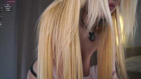 Video of a close-up of a blonde woman with straight, shoulder-length hair, wearing a black bra. Her face is partially visible, with a soft focus on her hair and the background.