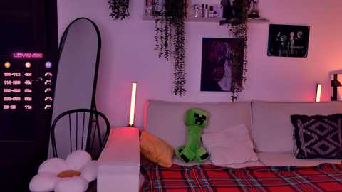 Video of a cozy, dimly lit bedroom with a Minecraft-themed decor, featuring a white bed with a green Creeper plush toy, plaid blanket, and a large wall-mounted TV displaying a Minecraft clock.