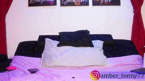 A video of a bedroom with a dark blue bed, white pillow, and red curtains. A pink vibrator and smartphone are on the bed.