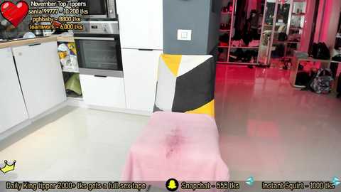 Video of a modern, colorful kitchen with a pink sheet covering a table in the foreground, yellow and black striped wall, white cabinets, and a red-lit closet in the background.
