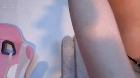 A video showing a close-up of a person's bare leg and a phallic object, partially obscured by a pink and blue toy chair in the background.