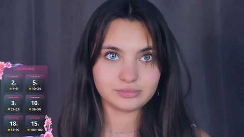 A video of a young woman with long, dark hair and blue eyes, wearing a pink top, against a dark background. To the left, a digital interface displays makeup options and statistics.