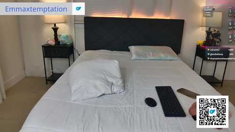 Video of a modern bedroom with a white bed, black headboard, pillows, lamp, phone, and framed artwork on the wall.