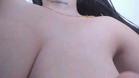 Video of a topless woman with large breasts, fair skin, and long dark hair. She wears a delicate gold necklace. Tattoo of \"very club\" visible on her neck.