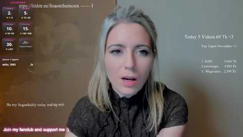 A video of a young woman with fair skin and long blonde hair, wearing a black shirt, speaking into a webcam. The background features a blurred, muted beige wall. Text overlays include a YouTube video link and a caption.