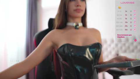 Video of a woman in a shiny black leather corset, holding a clipboard, with a white collar, in a modern office setting.