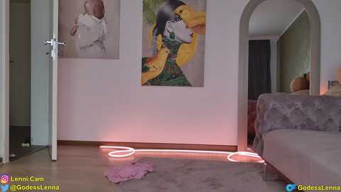 Video of a modern living room with a cozy, grey sofa, colorful abstract paintings, and a glowing neon light. The room has a minimalist, chic aesthetic.