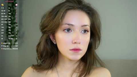 A video of a young woman with fair skin and wavy, shoulder-length brown hair, wearing a strapless top, set against a blurred background.