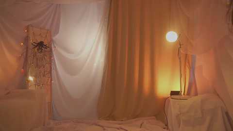 A video of a softly lit, dreamy bedroom with sheer white curtains, a cozy lamp, and a rustic wooden shelf.