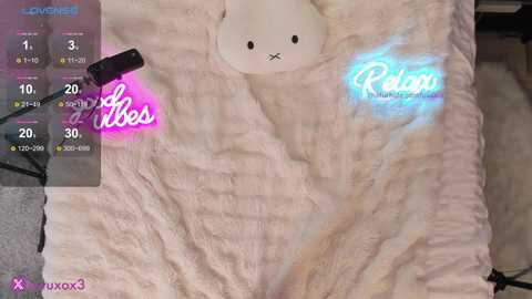 Video of a plush teddy bear with a white body and a blue glow, lying on a soft, fluffy blanket. Text overlay shows temperature and humidity levels.