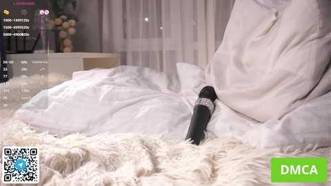 A video shows a person wearing a white robe, reclining on a plush white rug. A black dildo is partially visible under the robe. The background includes a TV screen with live stream details, a potted plant, and a window.