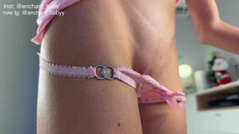 A video showing a close-up of a woman's lower torso, wearing pink lace panties with a silver clasp, in a brightly lit room.