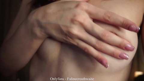Video of a light-skinned woman's bare breasts, with her left hand covering her right breast. Her fingernails are painted a glossy, pale pink. Text at the bottom reads \"OnlyFans: @Plumecoshawtie.\