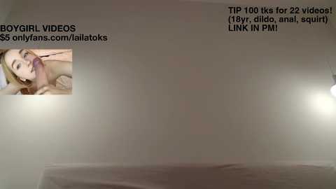 Video of a blonde woman with large breasts, lying on a bed, with a blurred background. Text overlays include \"BOY-GIRL VIDEOS\" and \"TIP 100 k for 22 videos (18, 18, anal, squirt).\