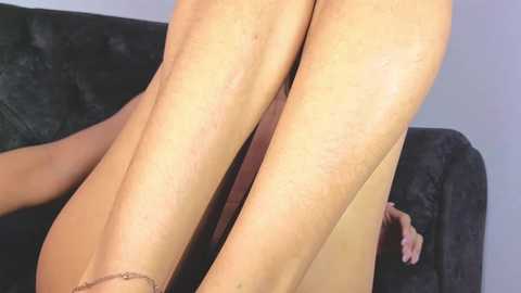 Video of a close-up view of a person's legs, lying on a black couch. The legs are smooth and light-skinned, with a slight tan, and the person's feet are visible, wearing brown sandals.