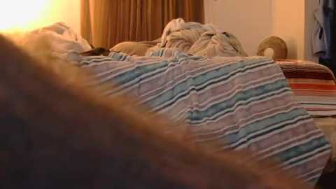 Video of a cozy, dimly lit bedroom with a person sleeping under a striped blanket, surrounded by soft, warm lighting.