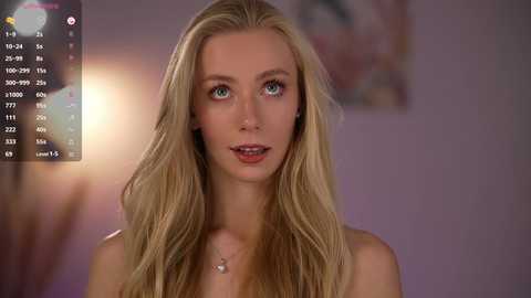 Media: Video of a blonde, fair-skinned woman with blue eyes and long hair, wearing a strapless top, indoors with blurred background.