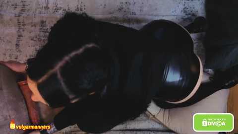 Media: Video of a black Labrador retriever lying on a gray, textured surface, wearing a shiny black leather collar. The background shows a blurred, dimly lit room.