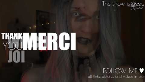 A dimly lit video featuring a pale-skinned woman with long, gray-streaked hair and dark makeup, wearing a gothic outfit. Text overlays read \"Thank You MERCI,\" \"The show is over,\" and \"Follow Me.\