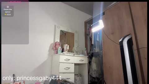 Video of a cluttered, dimly lit bathroom with a white vanity, mirror, toiletries, and a standing lamp.