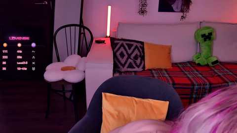 Video of a cozy, pink-themed room with a bed adorned with plaid and plush toys, featuring a Minecraft figure, a fluffy chair, and a glowing lamp.