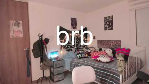 Video of a cluttered, small bedroom with a metal-framed bed, a white chair, and various personal items, including a stuffed animal and a doll.