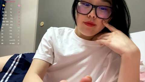 Video of an East Asian woman with straight black hair, wearing glasses and a white t-shirt, resting her head on her hand.