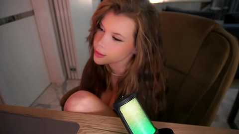 Media: Video of a fair-skinned, red-haired woman with large breasts, wearing headphones, sitting at a wooden desk in a dimly lit room.