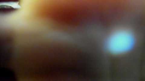 The image is a blurry video, featuring indistinct figures and objects in a dimly lit room with a warm, yellowish light. The background is out of focus, making it difficult to discern specific details.