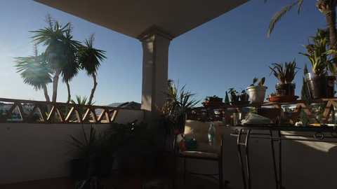 Video of a sunny balcony with potted plants, wooden furniture, and a clear blue sky.