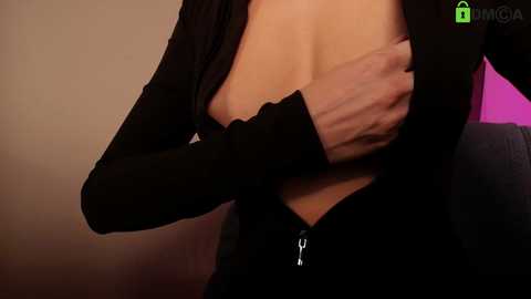 Video of a light-skinned woman with medium-sized breasts, partially exposed by her black cardigan, her hand covering her nipple. Background is a blurred beige wall with a green \"MGA\" watermark.