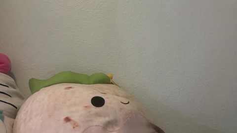 Video of a stuffed white bear with pink spots, wearing a green bow, resting against a textured light blue wall. The bear's black nose and small eyes are visible.