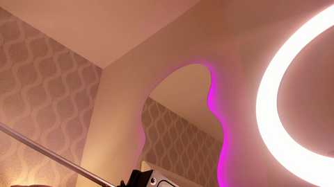 Video of a modern bathroom with a large, round mirror lit by a bright circular light, featuring a purple glow. The background shows a patterned wallpaper with white and beige hexagonal shapes.
