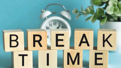Video of wooden cubes spelling \"BREAK TIME\" in black letters against a light blue background, with a silver alarm clock and a potted plant in the background.