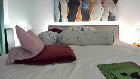 A video of a cozy, modern bedroom with a white bed, red and pink pillows, a white crib with butterflies, and abstract wall art in warm colors.