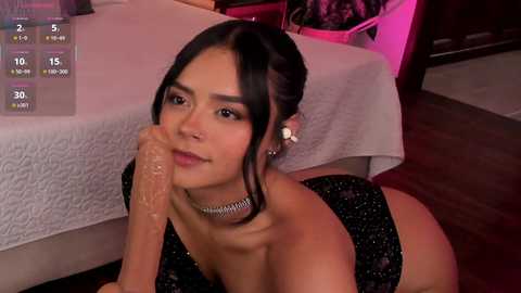 Video of a young Asian woman with fair skin, black hair, and dark eyes, lying on a white bed, wearing a black, sparkly dress, looking pensive.