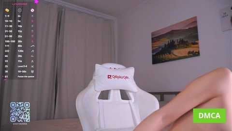 A video of a modern living room featuring a white ergonomic chair with a plush headrest, a wall-mounted painting of a serene landscape, and a person's hand in the foreground.