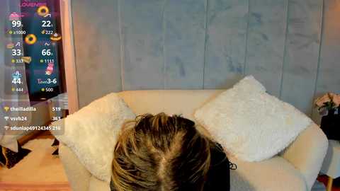 A video of a woman with brown hair, sitting on a plush white chair, against a light blue textured wall. Weather forecast overlay shows 69\u00b0F with a partly cloudy sky.